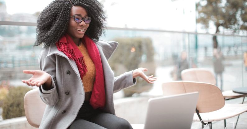 Video Content - Happy excited African American female laughing and gesticulating while having video calling on laptop and sitting at modern cafe